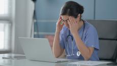 Nurse sitting in front of laptop with hands to head